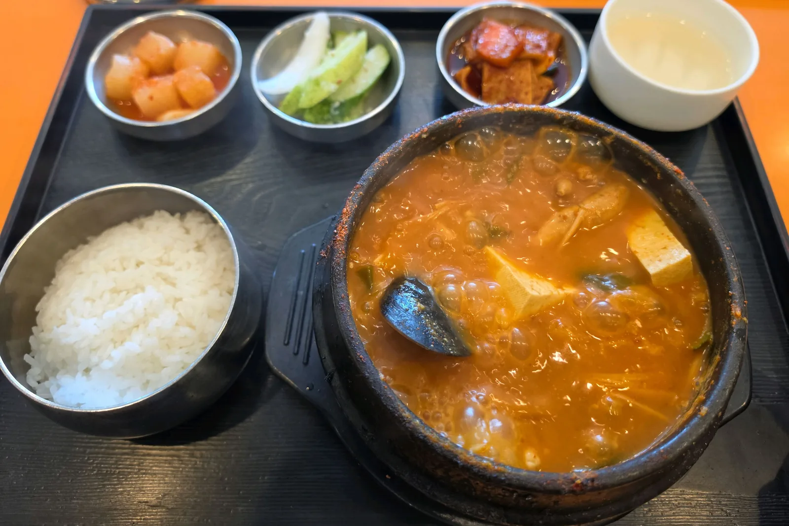 보글보글 끓는 알탕 뚝배기와 밥, 깍두기·오이·어묵 반찬, 흰 컵이 놓인 쟁반