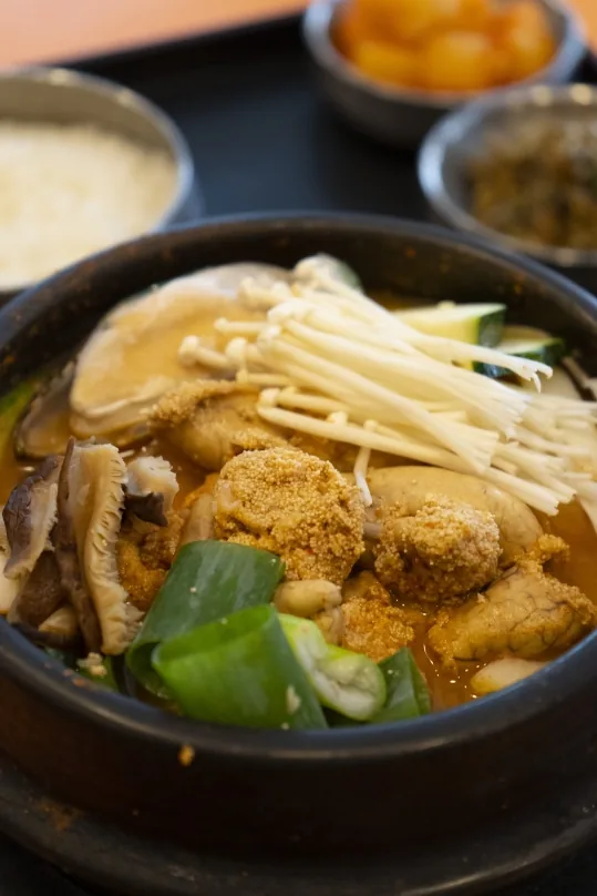 알탕 뚝배기 가까이(세로) — 알, 팽이버섯, 대파, 버섯 조각, 뒤로 밥과 반찬
